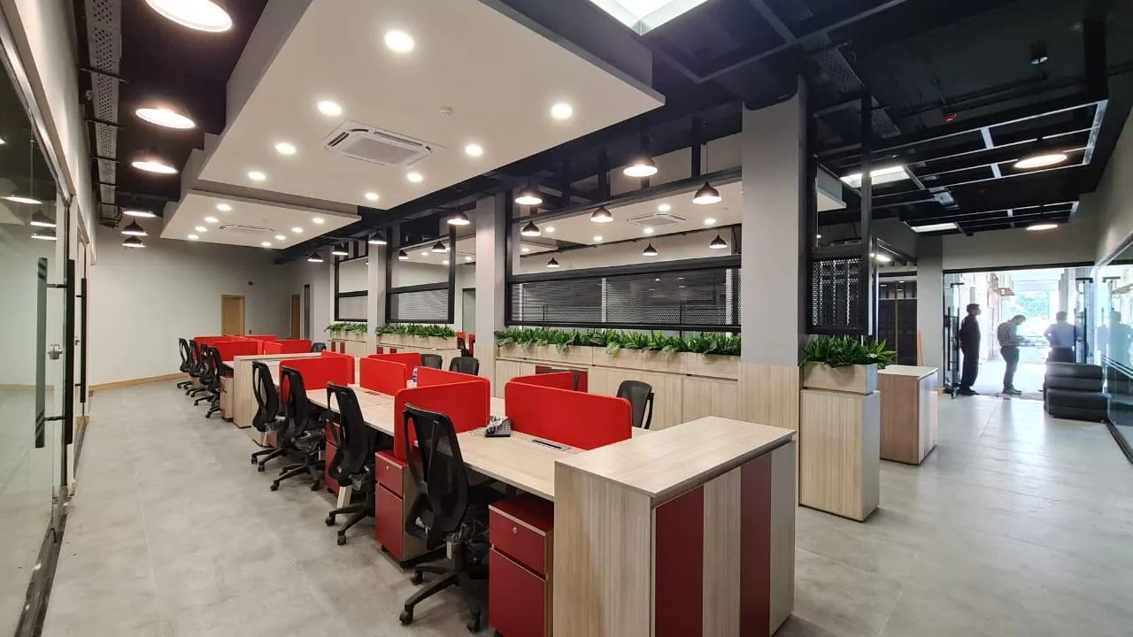 Open-plan desking in red and timber tones beneath an exposed ceiling grid