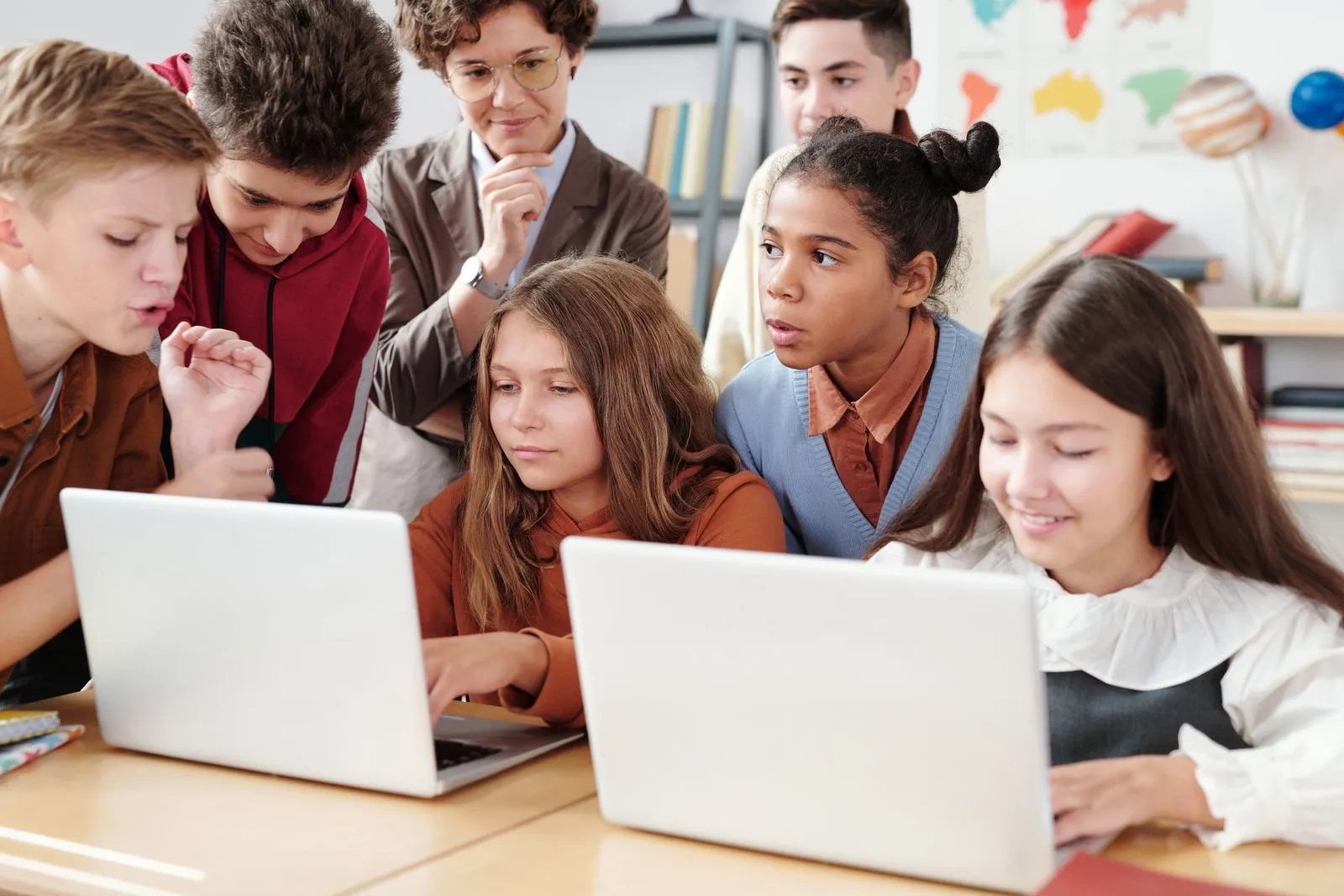 A teacher guiding students working together on laptops in a classroom